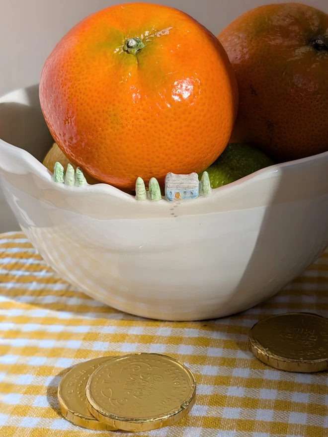 Handmade ceramic white bowl with a tiny blue house and tree details on the rim and white glaze on a yellow gingham table cloth