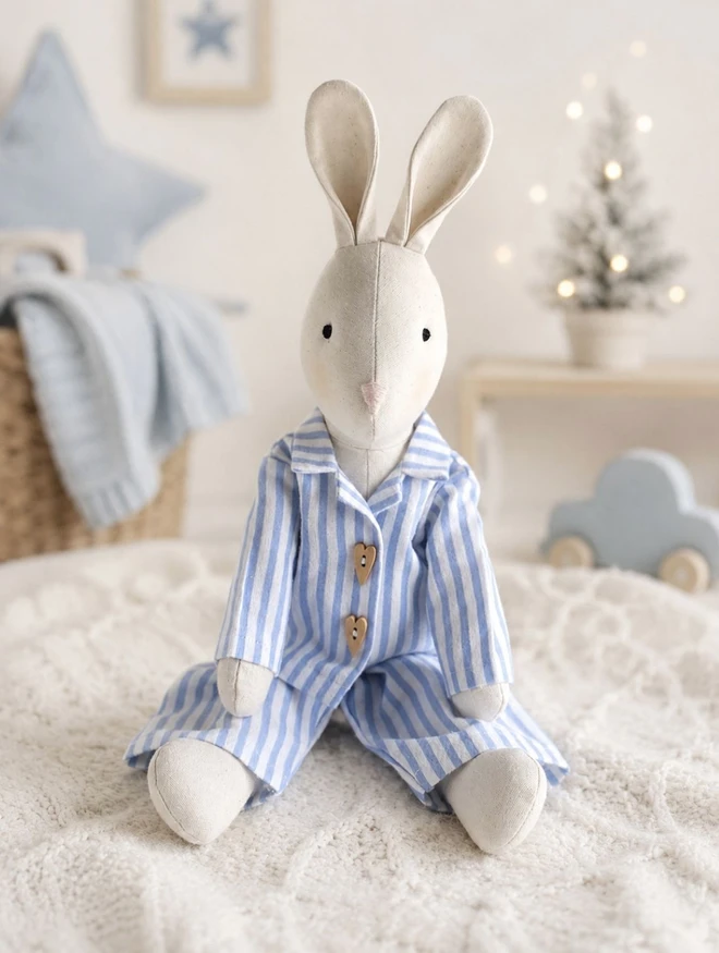 Handmade Gerald Bunny wearing blue and white striped pyjamas in a pale Christmas nursery with soft twinkle lights, by Verity Isabelle.