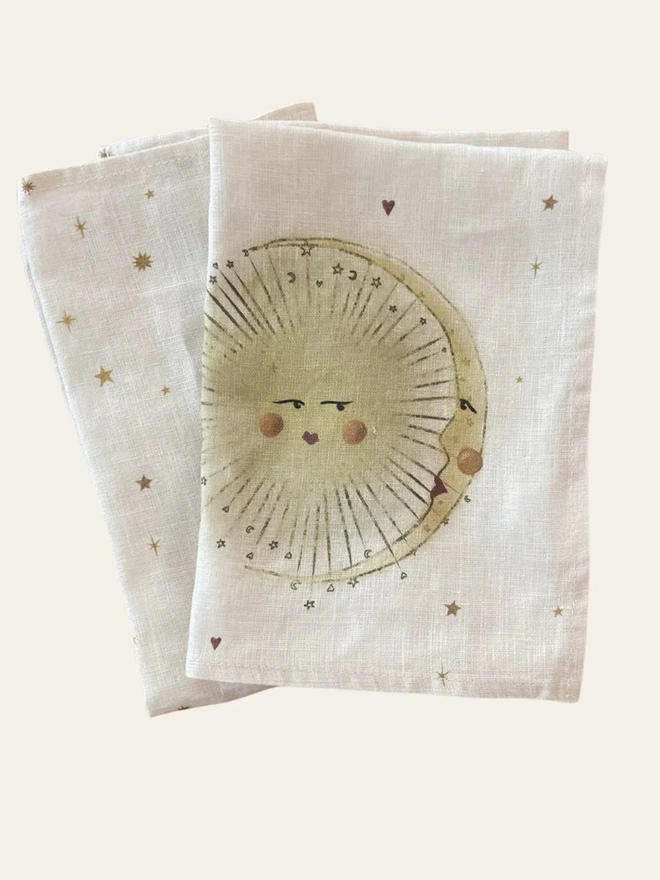 Celestial Linen Dinner Napkins (Set Of 2)), a linen napkin with a sun motif sitting on a plain white surface. 