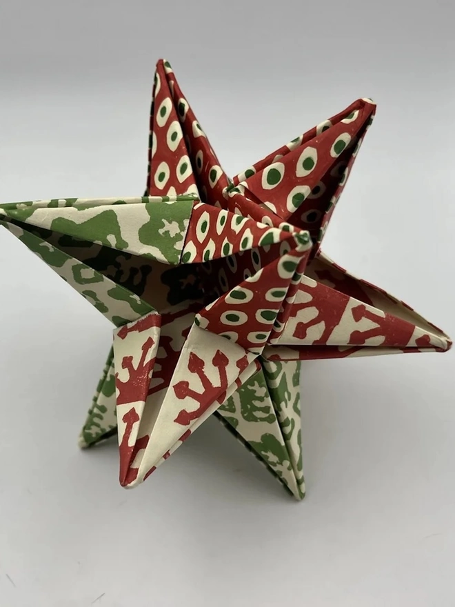 Colourful Star Kit. A finished origami paper star folded from red and green patterned papers, shown against a plain white background. The 3D star ornament combines spot, sunburst and leaf prints for a handmade Christmas decoration.