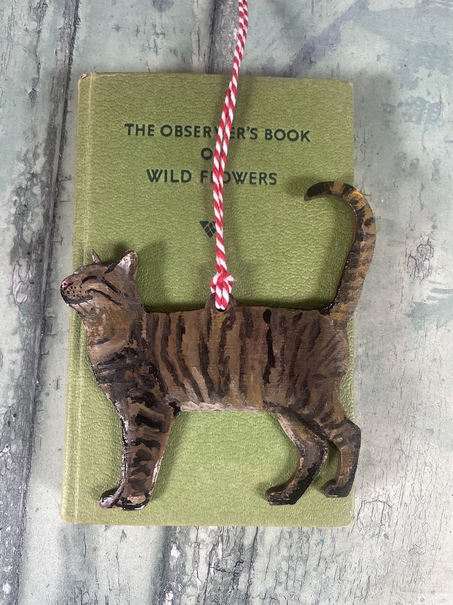 Tabby Cat Christmas Decoration with red and white twine placed onto a book about cats 