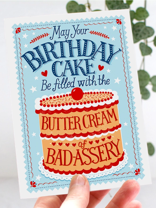 badass birthday cake card in a hand with a plant in background