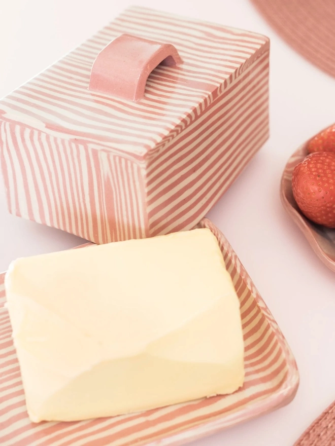 Striped Butter Dish, a colourful striped butter dish sitting on a white surface. It is accompanied by other striped dishes and food. 