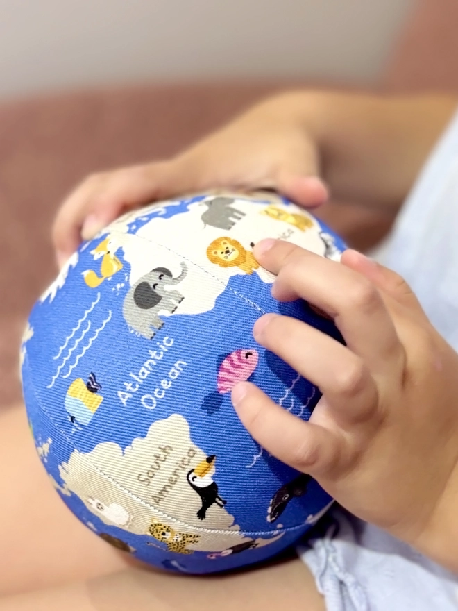Girl holding first globe soft toy and the guide that comes with it. She is pointing at a Lion on the globe