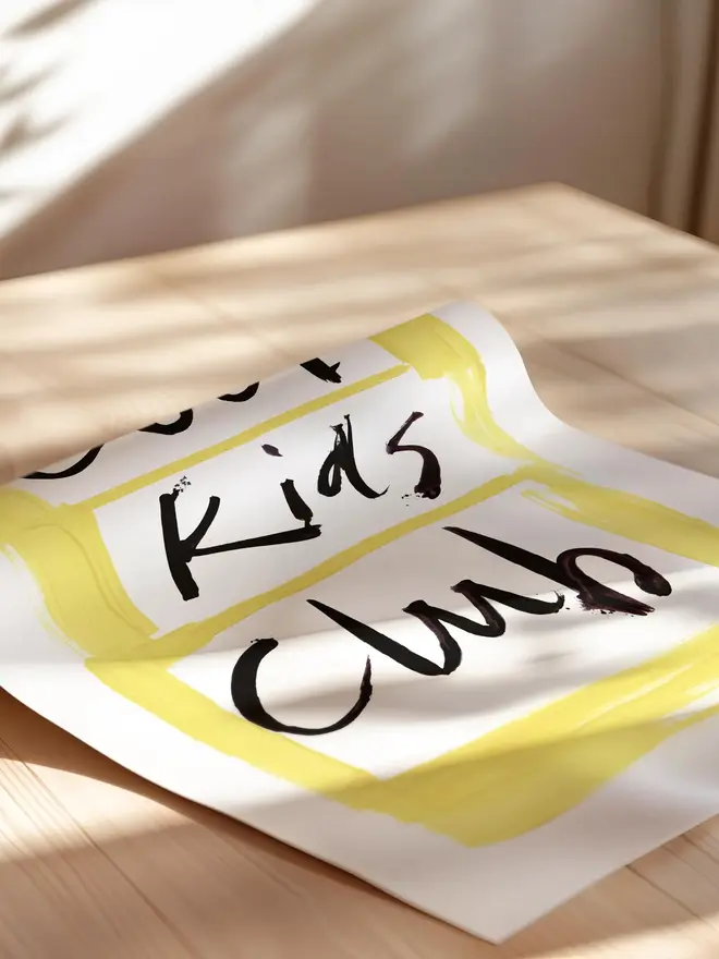 'cool kids club' art print. a print with a white and yellow background with a slogan in black lettering being rolled up.