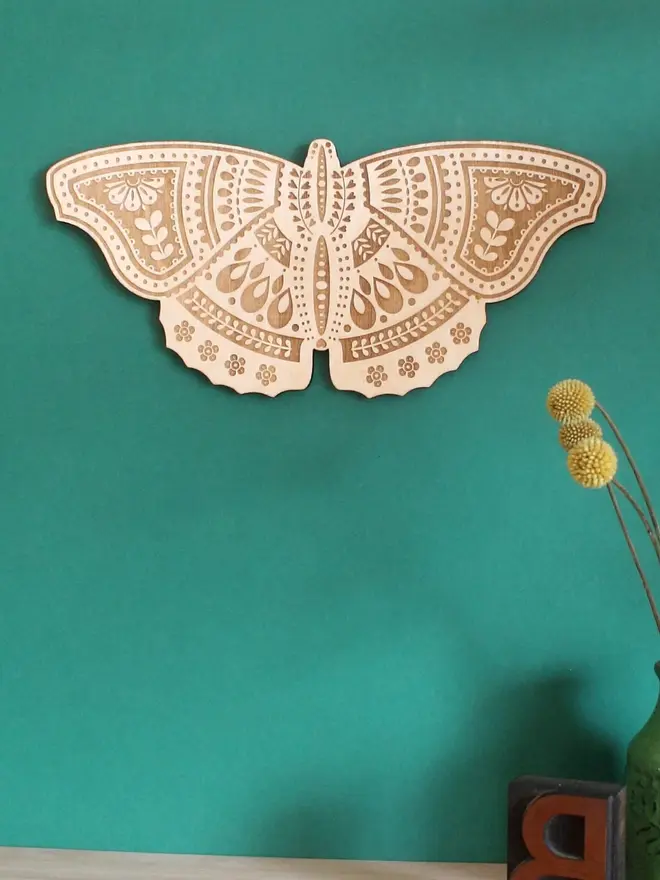 Wooden Folk Art Butterfly Hanging Decoration, wooden insect decoration hanging on a green wall. 
