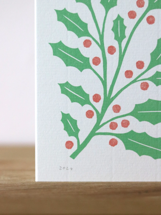A Christmas card featuring a reproduction of an original linocut print of holly
