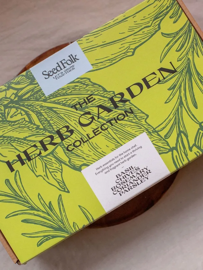 the Herb garden seed starter kit. box in a decorative green sleeve photographed on wooden dish.