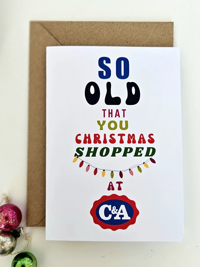 A photograph of the front of a humorous A6 greeting card illustrated using brightly coloured text and the retro shop logo. The text says so old that you Christmas shopped at C&A with string lights