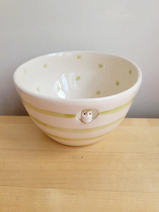 a green and cream spotty bowl with stripes and a little modelled owl inside a circular cut out on a wooden work top