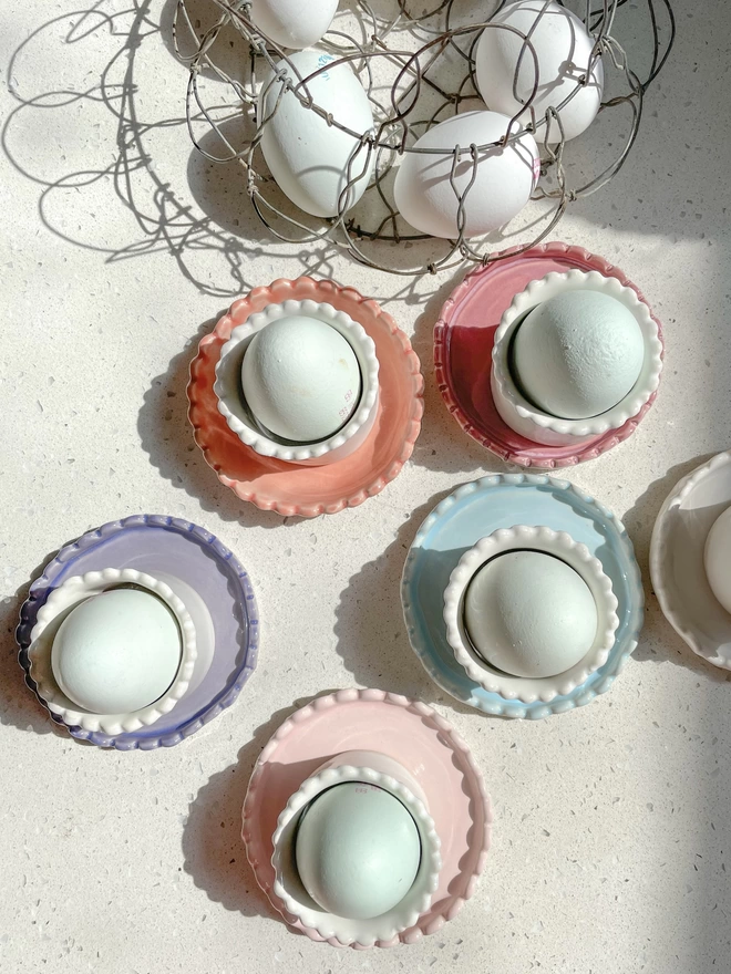 top down photo of white scalloped edge egg cups with eggs in sitting on a variety of ceramic coasters