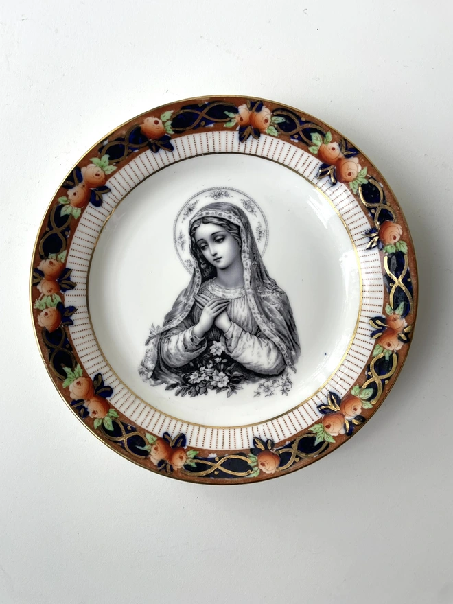 a vintage plate with a really ornate border has the victorian black and white illustration of the virgin mary in the centre