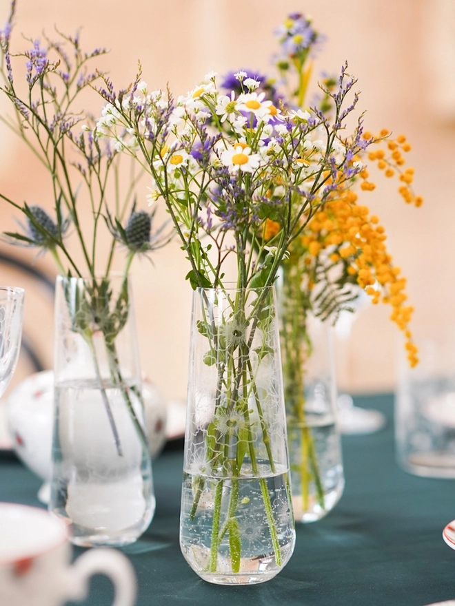 Floral Twist crystal bud vase holding colourful wildflower arrangements placed on a dark green tablecloth.