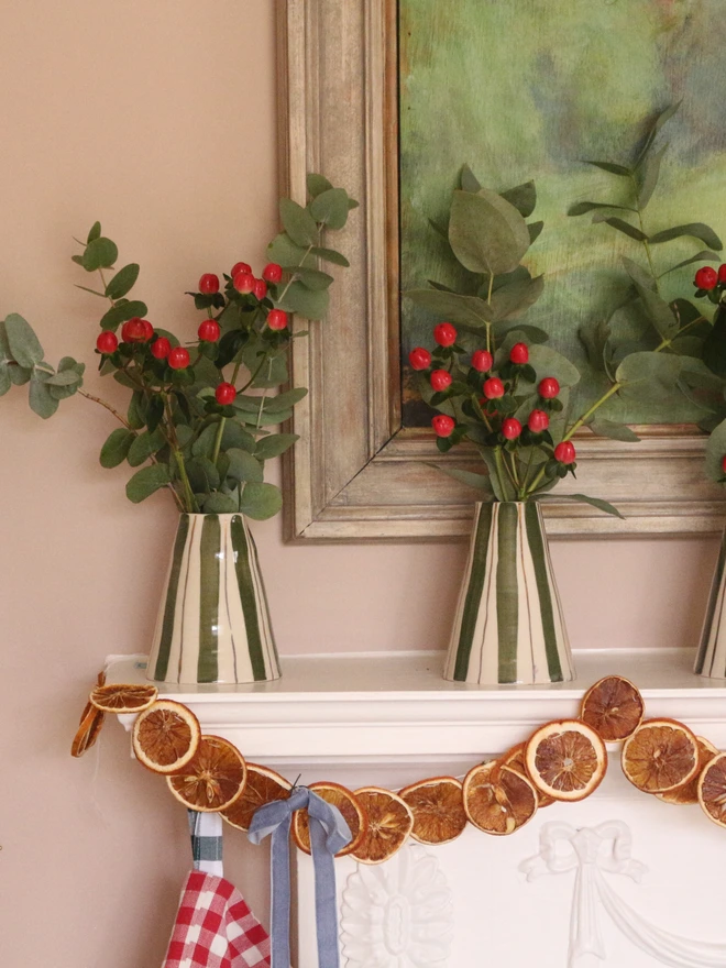 Two christmas vases with green and gold stripes and red berries in them