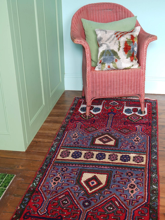 Multicoloured vintage rug with central turquoise stripes and green border on wooden floor