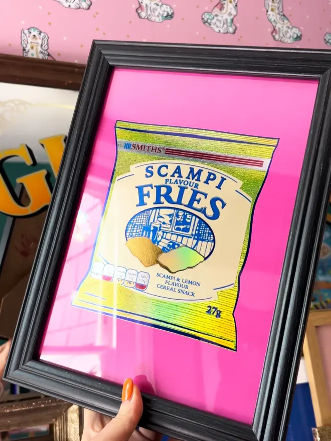 'Scampi Fries' ScreenPrint, a person holding a colourful scampi fries print in a frame. 