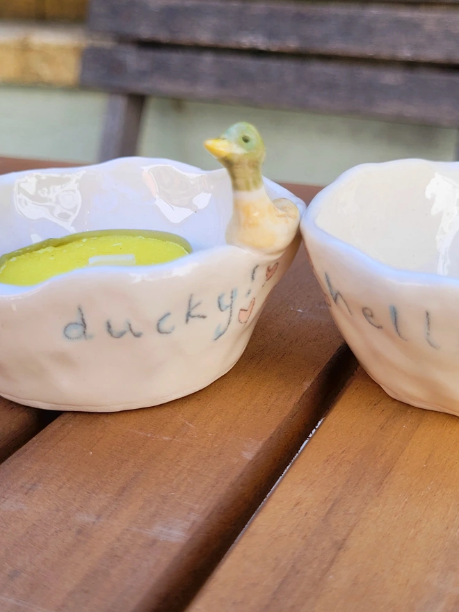 small ceramic ivory pot on a wooden table with a modelled drake duck on the rim and the words hello ducky on the pot
