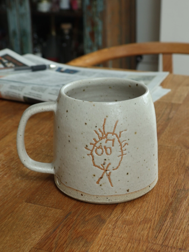 Childrens Drawing Handmade Ceramic Mug
 on wooden table with a newspaper in the background