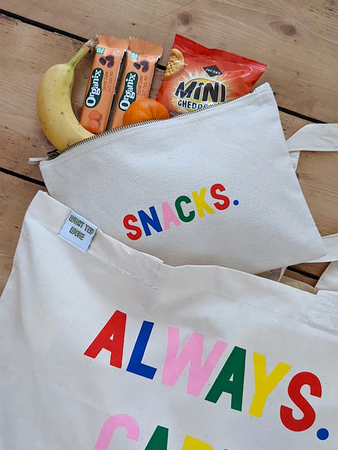 A canvas pouch on a wooden floor with multi coloured 'Snacks' slogan