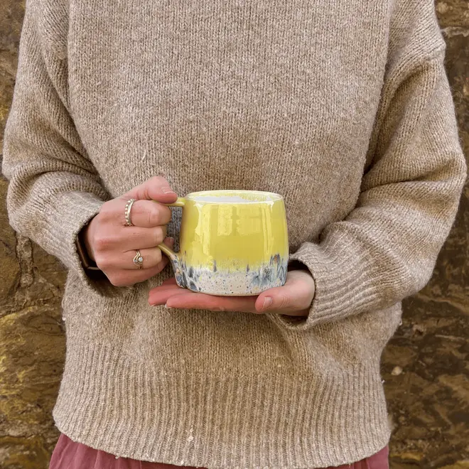 Shoreline Large Round Mug, a woman wearing a jumper holding a colourful mug in her hands in front of her. 