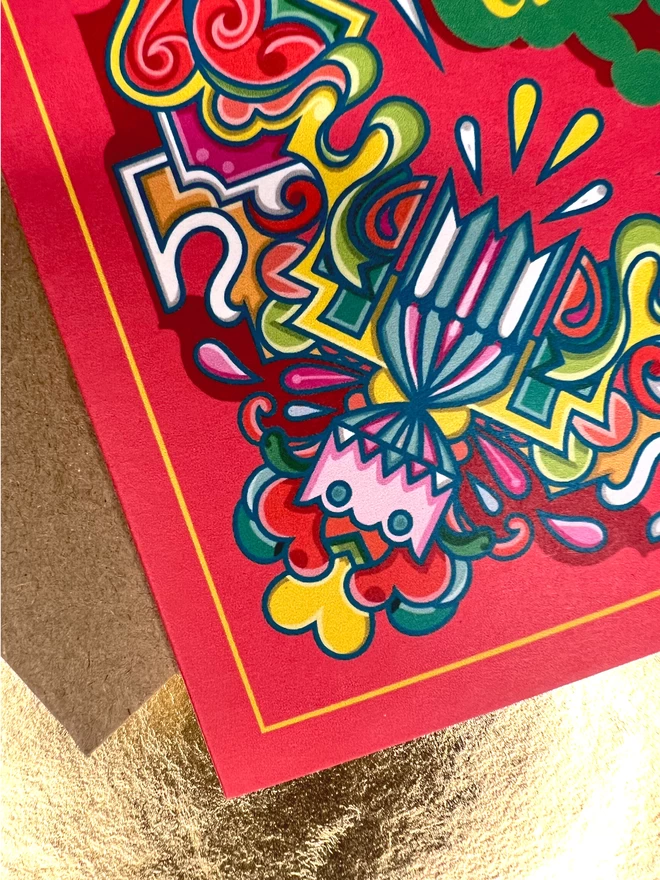 Corner detail of the card showing the red background, thin yellow border, multi-coloured exploding cracker and abstract surrounding design.