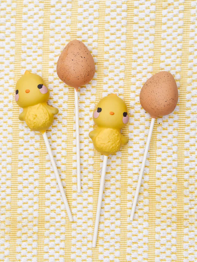 Easter Chick&Egg cake pops placed  against a white and yellow tablecloth 