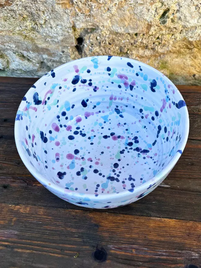 Sweetpea Small Bowl, a colourful bowl placed on a wooden surface against a brick wall. 