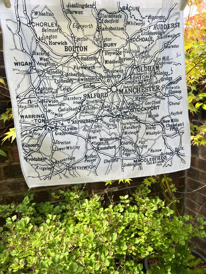 Mr.PS Greater Manchester Handkerchief hanging on a washing line with green plants and brick wall in the background