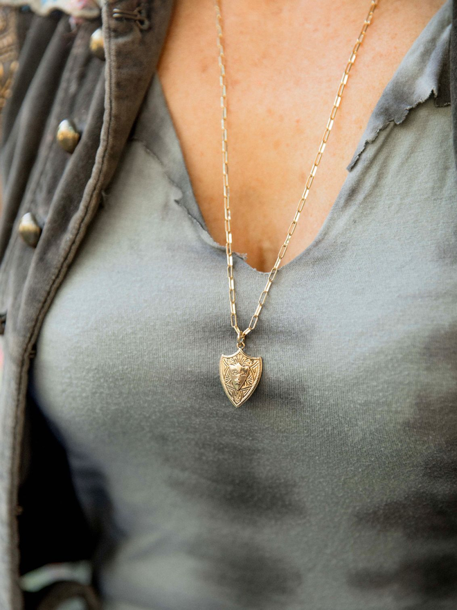 Close up of woman wearing a gold paperclip chain necklace with gold shield charm