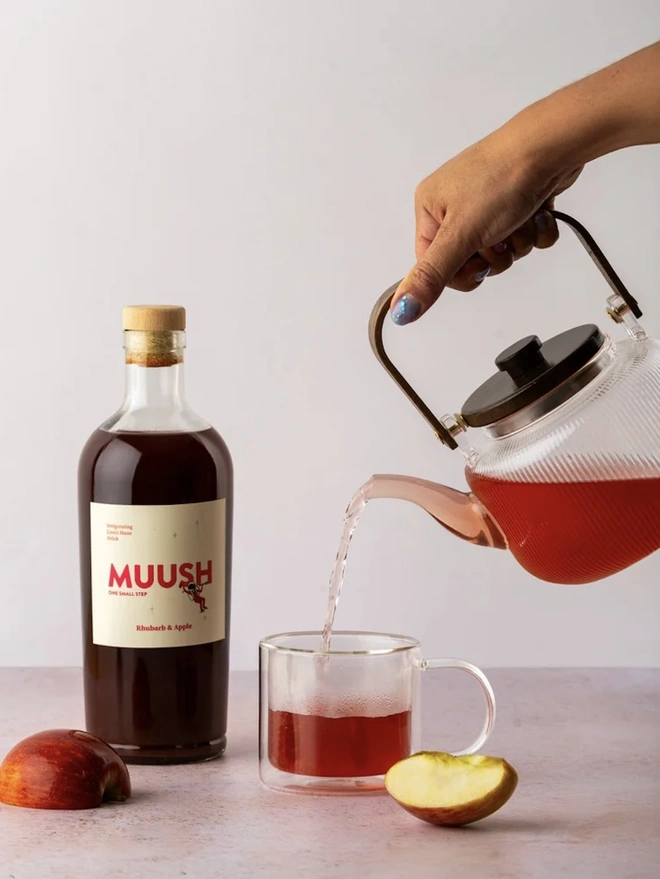 Rhubarb & Apple Elixir, a drink being poured sitting on a stone surface next to apple slices. 