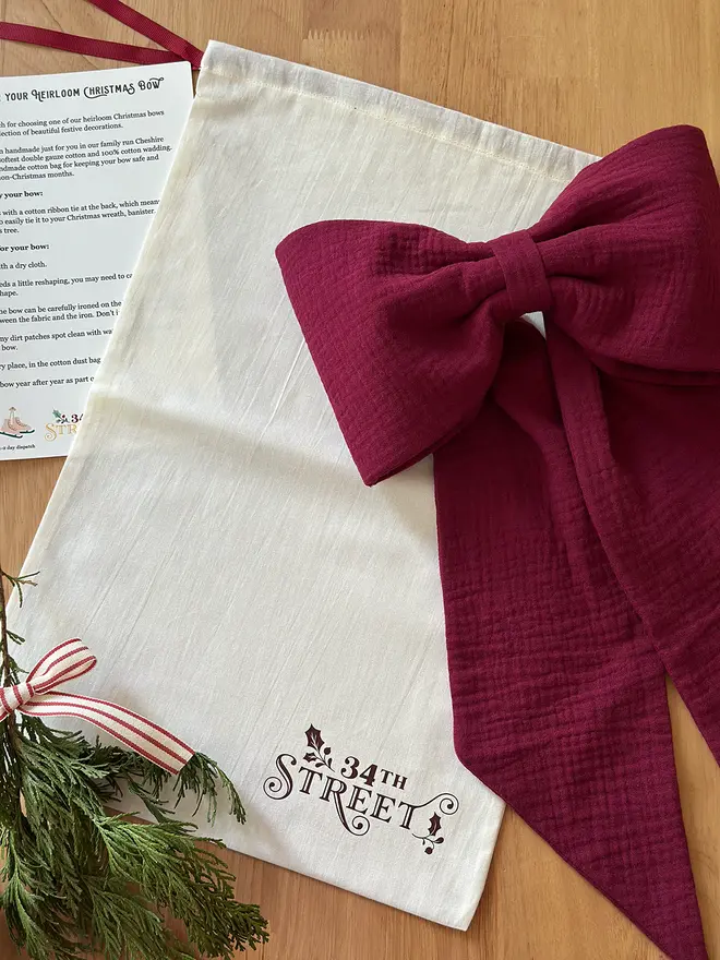A cotton bag with the 34th Street logo on lays on a wooden desk with a handmade Christmas bow beside it.