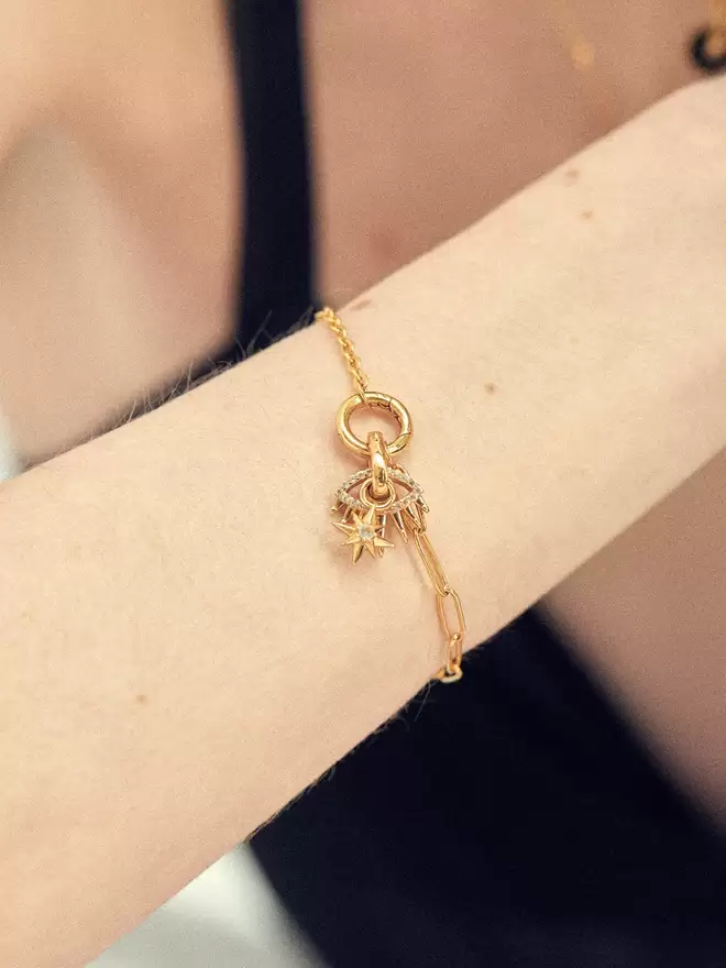Woman wearing a gold bracelet styled with an evil eye charm and a gold star charm