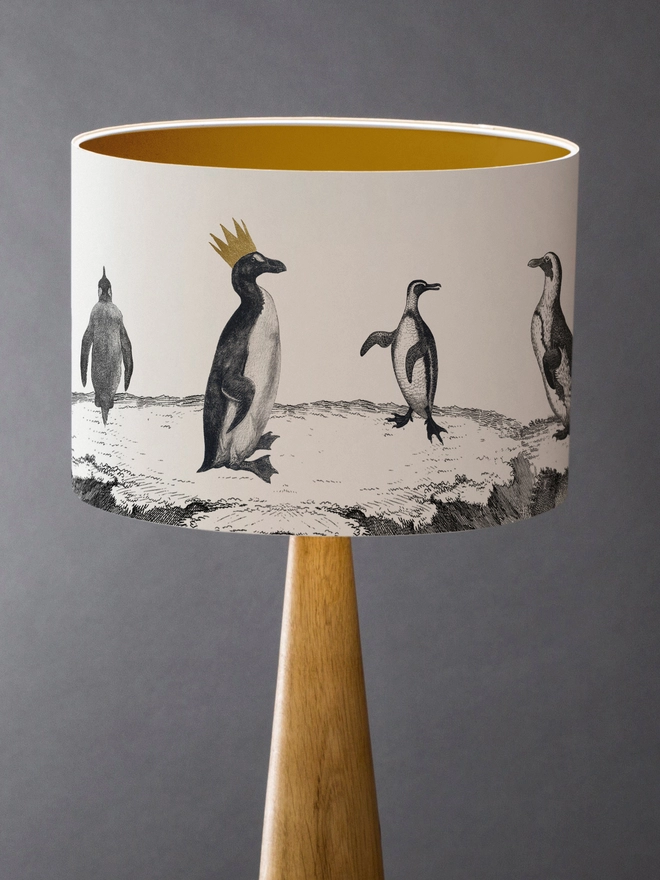 Drum Lampshade featuring a parade of penguins with a gold inner on a wooden base 
