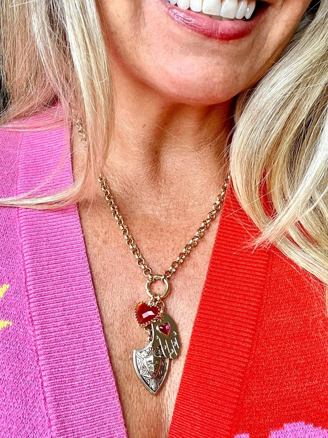 Woman wearing a gold charm necklace with a gold shield, a red heart and a hamsa hand