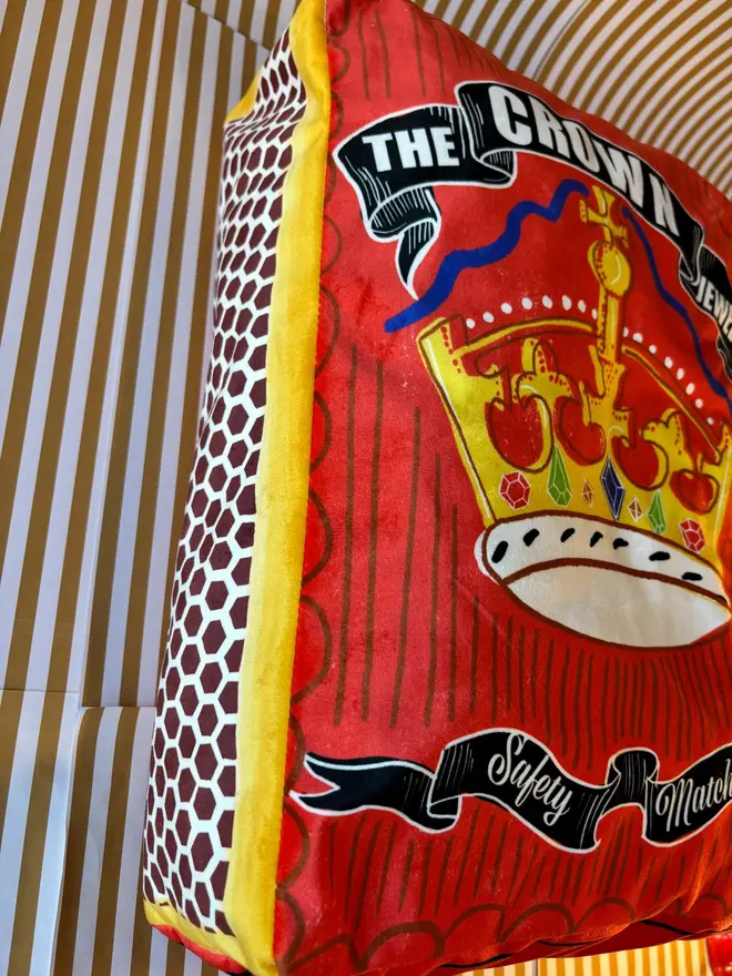 Crown Matchbox Cushion, a colourful red cushion sitting on a decorated surface. 