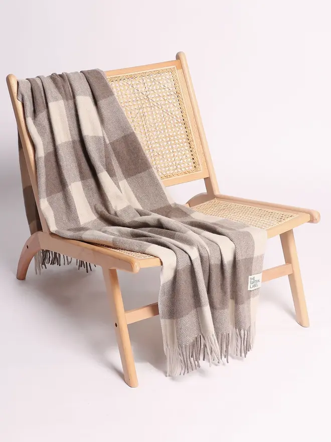 Jacob Blanket, a grey blanket draped over a wooden chair on a plain surface against a white backdrop. 