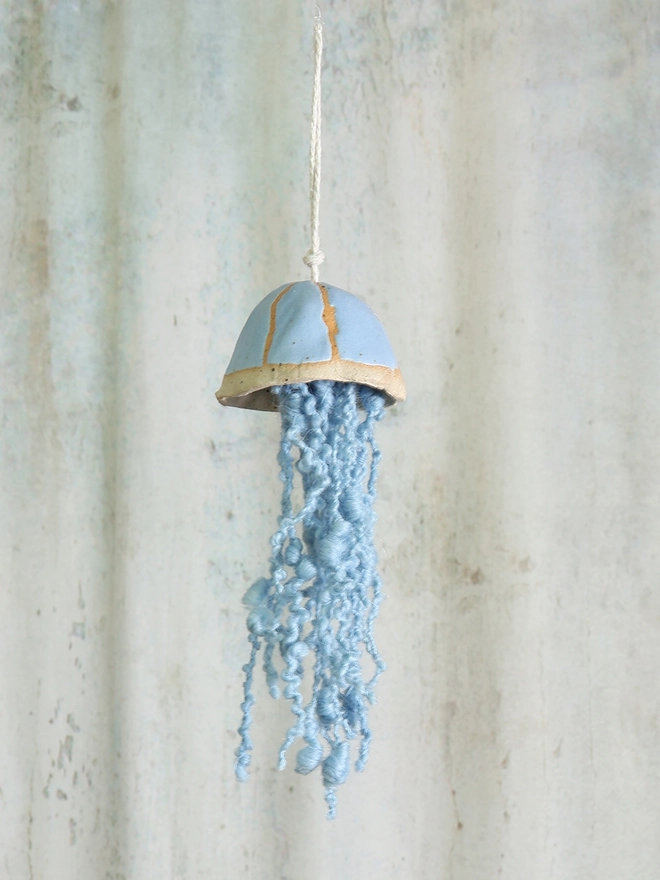 inky blue handmade ceramic jellyfish hanging hung infront of a pastel toned background curtain