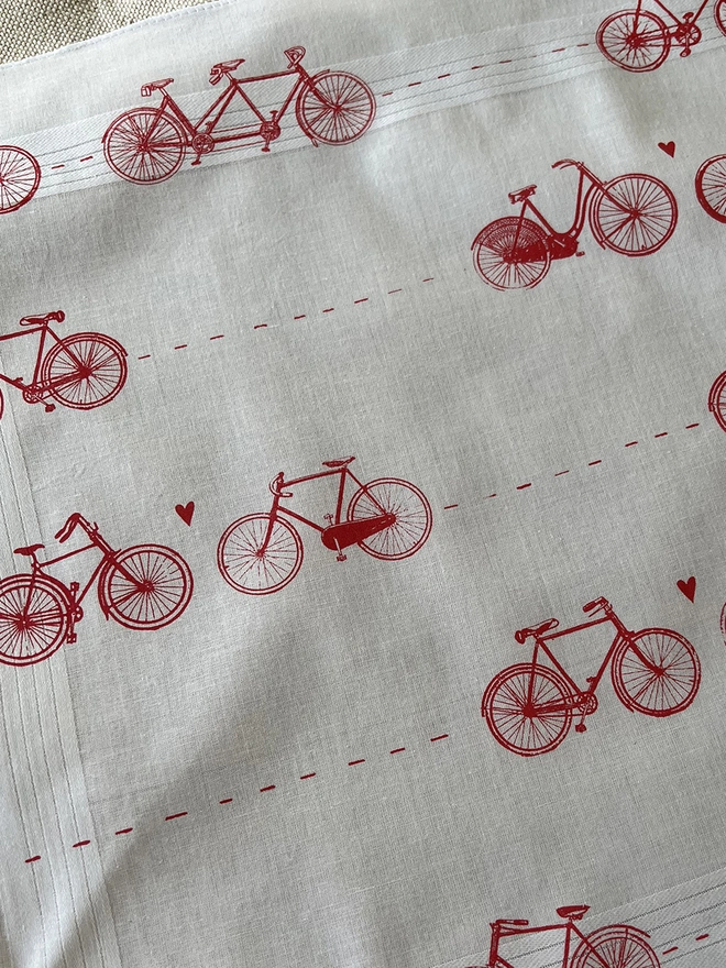 Detail of a Mr.PS white cotton handkerchief printed with a pattern of vintage bicycles with little hearts in coral red