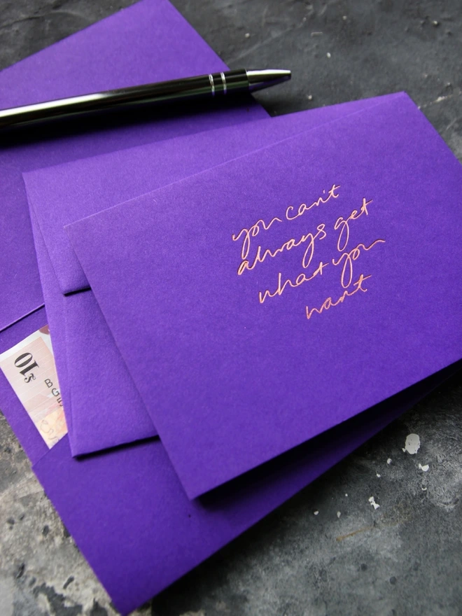 Hand foiled cash card or money wallet in a royal purple colour handfoiled in shiny rose gold foil text which says ‘You Can’t Always Get What You Want’.