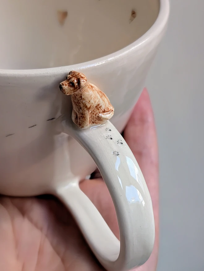 Fox red Labrador sculpture on the handle of an off white ceramic cup with tiny pawprints and hearts 