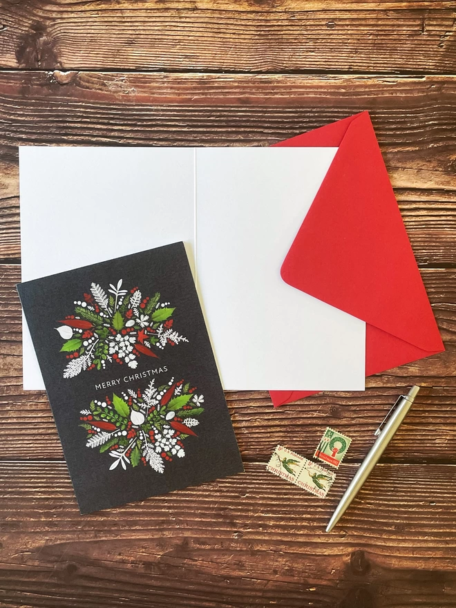 Christmas card with pressed festive foliage design on open card and red envelope - blank inside, wood background, vintage stamps, silver pen