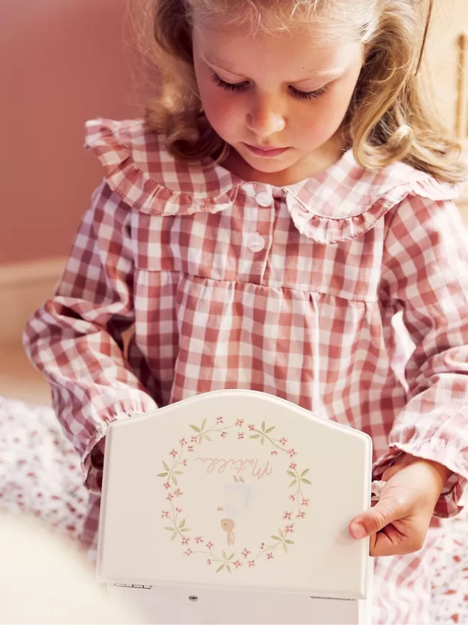 Personalised music box with a pink garland by Nells Archdale seen held by a child in a gingham dress.