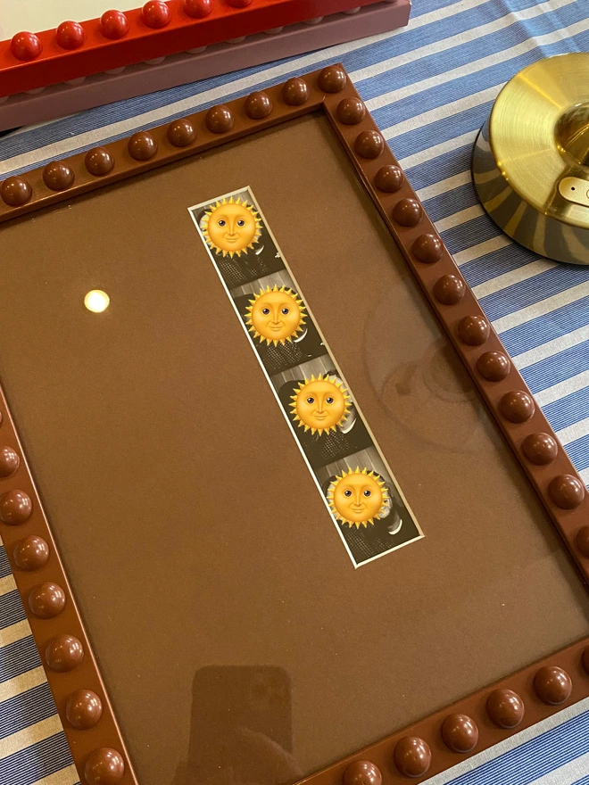 Brown photo strip / mount shown in a bobbin frame holding a strip of photographs from a photo booth