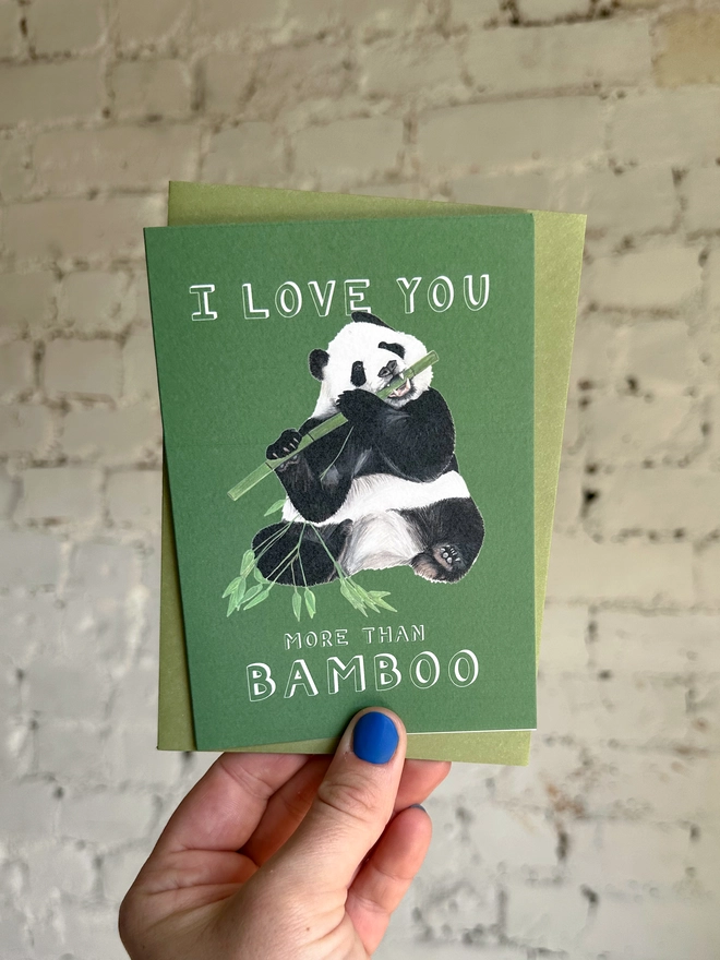 deep green card featuring a realistic illustration of a panda eating bamboo and the text "I Love You More Than Bamboo" with olive green envelope