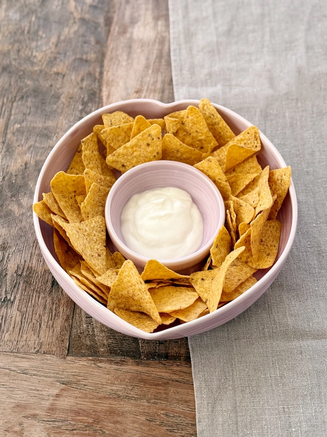 Heart shaped chip and dip bowl with tortilla chips and dip on a rustic wooden table