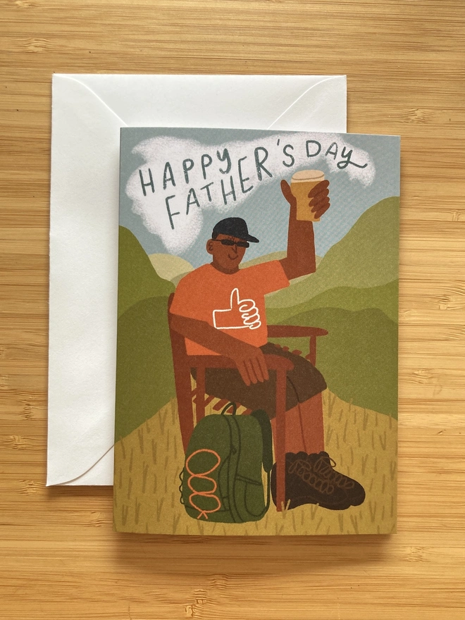 Illustrated greetings card of a dad holding up a pint, wearing hiking gear, sat in the country side. The text says 'Happy Father's Day'