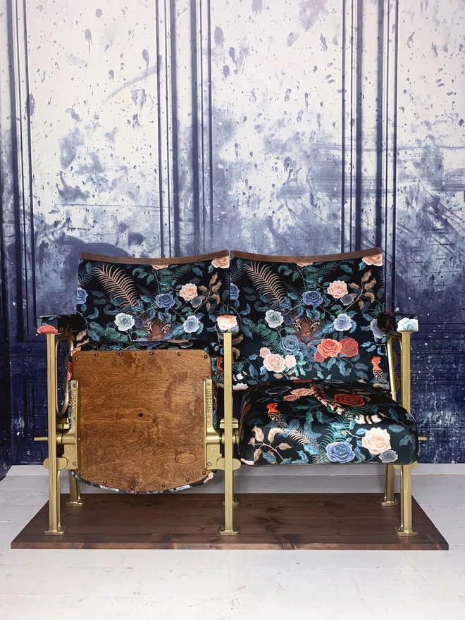 A set of two vintage cinema seats upholstered in a black floral velvet with a tiger peeking out behind the flowers. One seat is up and one seat is down.