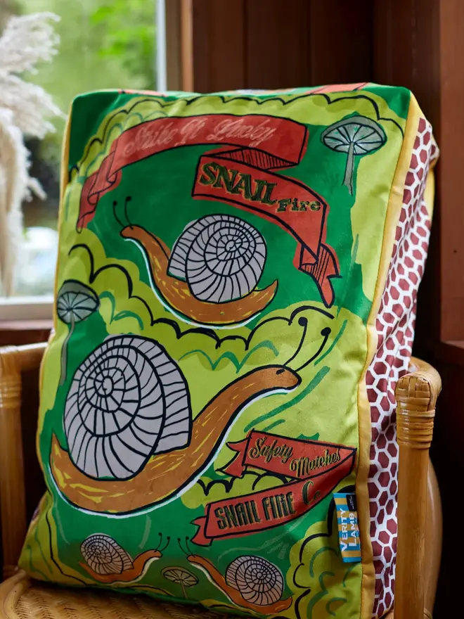 Snail Matchbox Cushion, a green decorated cushion sitting on a chair. 