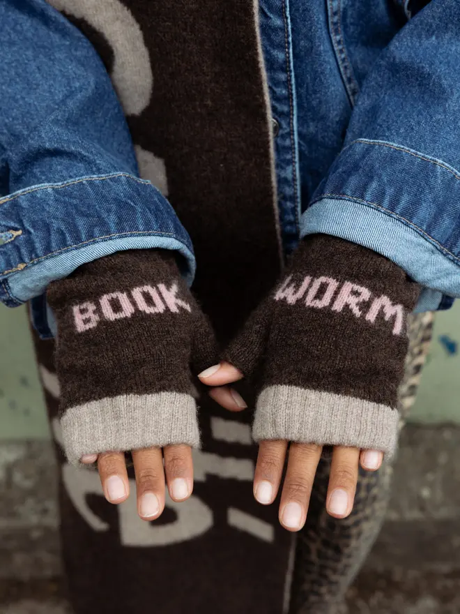 Lifestyle image of a person wearing the Cocoa & Calamine Book Worm Fingerless Mittens, with a denim jacket on