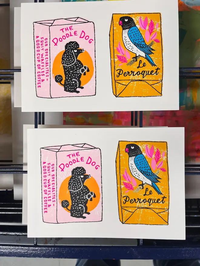Parrot And Poodle Sugar Cube Screenprint Sugar Sugar, a pair of colourful sugar cube designs, they sit on a studio rack. 